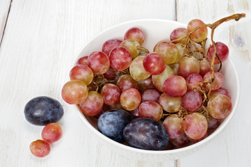 Plums and grapes in bowl on the white wooden table