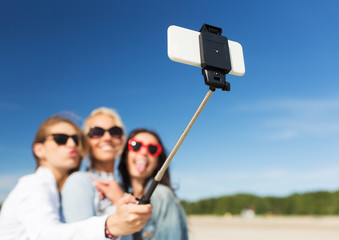 women with selfie stick and smartphone on beach