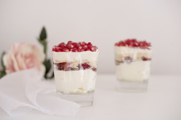 Homemade layered dessert with mascarpone, chocolate, cream, fresh strawberries, cookies, pomegranate. Cheese in a glass. White background, high key, selective focus