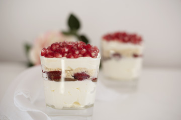 Homemade layered dessert with mascarpone, chocolate, cream, fresh strawberries, cookies, pomegranate. Cheese in a glass. White background, high key, selective focus