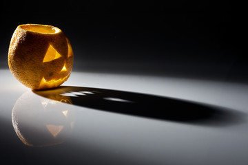 Food art creative concept. Halloween scary face carved into fruits and vegetables isolated with back light over a dark background. Text space.