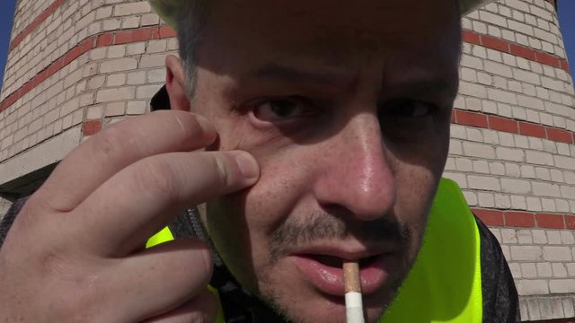 Worker with cigarette in mouth look to camera and touching eye