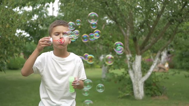 A cute boy blows the bubbles in the garden
