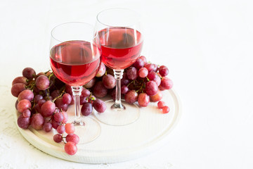 Two glasses of homemade rose wine and grapes on white wooden desk. Selective focus