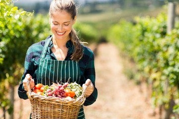 Happy female farmer holding a basket of vegetables