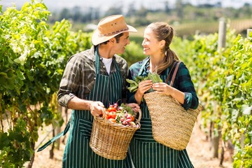 Happy farmer couple holding baskets of vegetables
