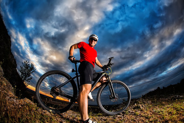 Fototapeta premium cyclist standing with mountain bike on trail at sunset