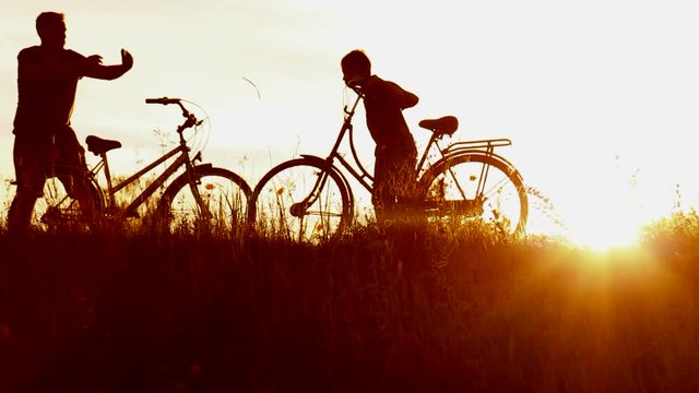 Happy father takes photos of little son near bikes in sunset lights. Family makes self portraits photos with cell phone in beautiful sunny landscape. Silhouettes of man, child over sky background