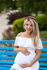 Naklejka premium Beautiful lovely girl wearing her first child in the stomach and is looking forward to his birth. Strolling in the park, enjoy nature and quietness
