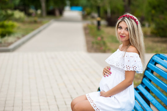 Beautiful lovely girl wearing her first child in the stomach and is looking forward to his birth. Strolling in the park, enjoy nature and quietness