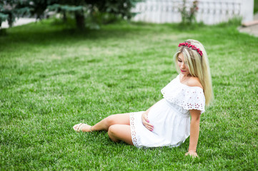 Fototapeta premium Beautiful lovely girl wearing her first child in the stomach and is looking forward to his birth. Strolling in the park, enjoy nature and quietness