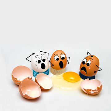 Cracked Eggs concept of three eggs surrounded by broken egg shells and yolk. Funny image with angry and sad faces on eggs while looking at the cracked eggs.  Egg Massacre.