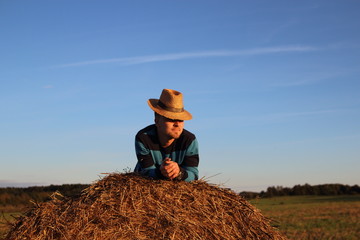 Naklejka na ściany i meble мужчина молодой у стога сена в поле в соломенной шляпе