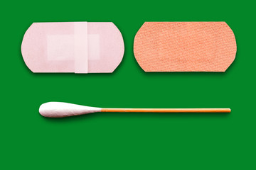 A cotton brush and two adhesive plasters, on green background
