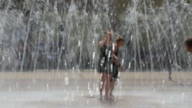 girls running and dancing through the fountain, images is blurred, no recognizable people