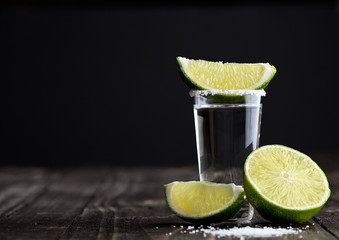 Tequila silver shot with lime slices and salt on wooden board