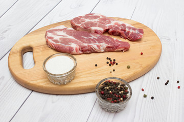 Two raw plump  pork neck chops with spices on wooden cutting board