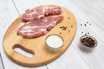 Two raw plump  pork neck chops with spices on wooden cutting board