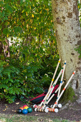 Croquet Set Leaning against and at foot of Tree.  Vertical.