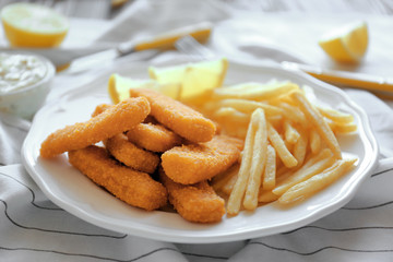 Tasty fish nuggets with lemon and fries on plate