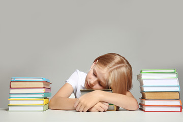 Cute girl sleeping on books on grey background