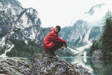 Man with red raincoat sitting on rocks with mountain and lake on the background - 121594467