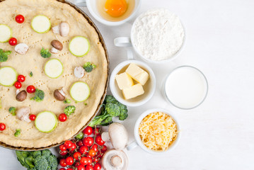 The selection of ingredients for the preparation of traditional French dishes quiche lorraine, on white wooden table with a baked dough in the baking dish in the cooking process, top view, copy space