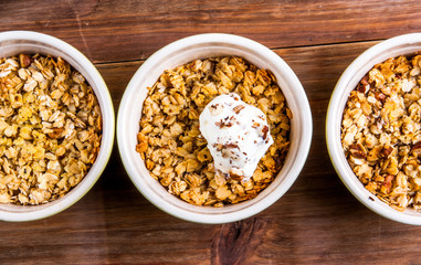 Three portion of freshly made autumn apple crumble with fresh green apples on a wooden table, top view