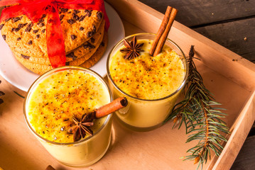 Traditional Christmas drink eggnog and cookies on a wooden background surrounded by Christmas tree branches. 