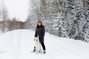 Woman with white swiss shepherd dog in winter forest