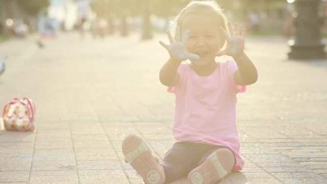 Cute girl soiled with chalk, having fun and show her dirty hands to the camera