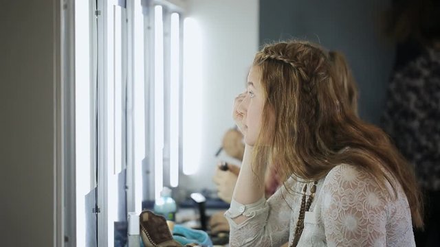 Three girls sit in front of mirror and are busy with smartening up.