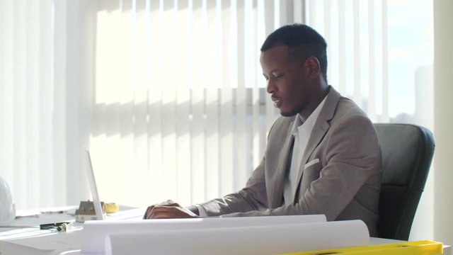 Black young businessman using laptop computer sitting in a modern white office