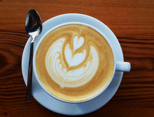 A Cup of hot latte art coffee on wooden background with natural lighting. A cup of tasty latte art coffee with flower pattern. Hot milk art coffee on wooden table.