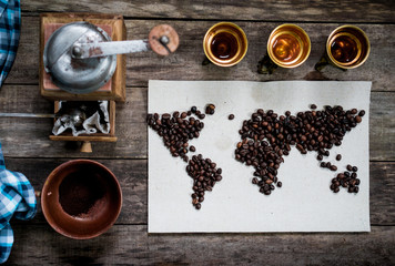 map of the world, lined with coffee beans on old paper. Eurasia, America, Australia, Africa. vintage. Black coffee, ground coffee, cognac, old hand grinder on old wooden table . top view. flat lay