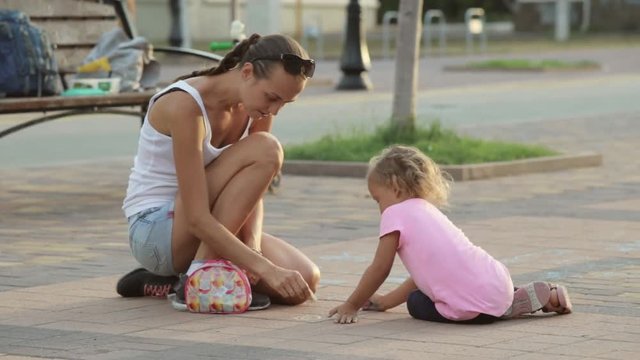 Cute girl and her mother drawing with chalk on sidewalk