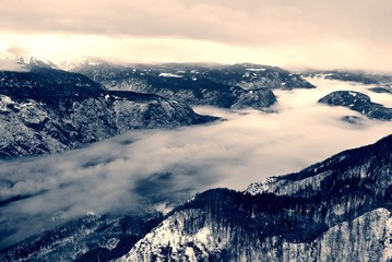 Panoramic view over the snow-covered mountain tops wrapped in fog. Monochrome image filtered in retro, vintage style with soft focus and red filter; nostalgic winter landscape. - 121616811