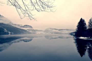 Snowy winter landscape on the lake in black and white. Monochrome image filtered in retro, vintage style with soft focus, red filter and some noise; nostalgic concept of winter. Lake Bohinj, Slovenia.