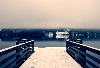 Snow covered wooden jetty on the lake; foggy winter landscape in black and white. Monochrome image filtered in retro, vintage style with soft focus and red filter. Lake Bohinj, Slovenia. - 121616899