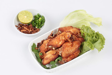 Deep fried chicken topped fried sliced red onion served with side dish as halve green lemon ,minced shallots and filled fried red onion on white. Side view.