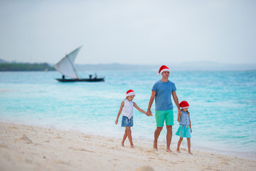 Young father and little girls in Santa hat on the beach