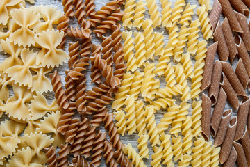 Background of mixed two colored pasta on grey wooden. Raw  frame. Copy space.