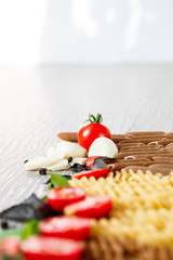 Mixed of two colored pasta near tomatoes, garlic and basil on grey wooden  background. Close up  raw . Copy space.