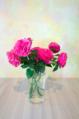 pink roses in a glass vase on a wooden table on a background of pale yellow walls