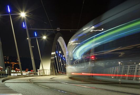 Tram speeding over a bridge in Lyon at dusk.