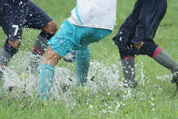 Young girls playing soccer in the rain on a wet grassy field