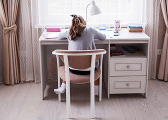 Little school girl doing homework in her room, view from the back
