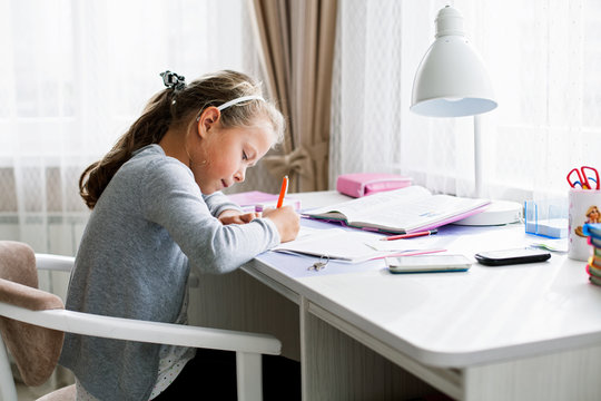 Little school girl writing something in an exercise book, doing homework.