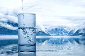 Fototapeten Wasser in ein Glas gießen gegen die Naturlandschaft mit See und Bergen © dash1502