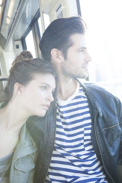 Couple riding train together, looking out window